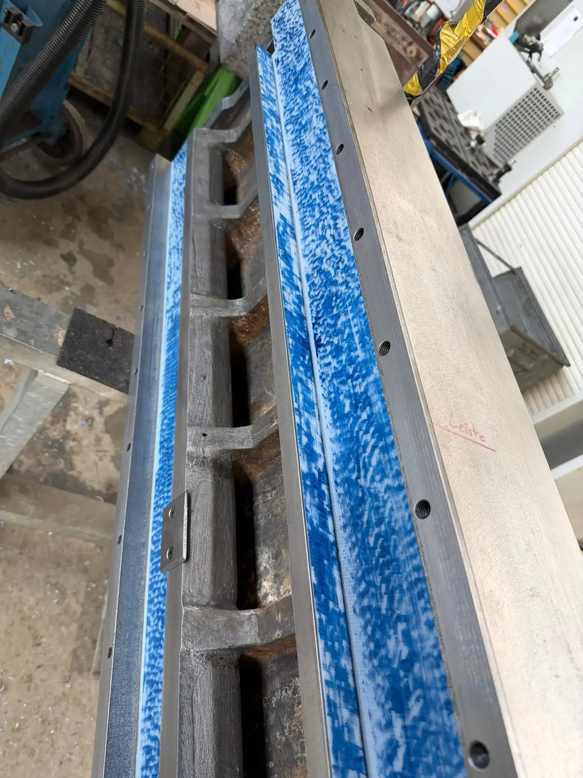 Zwei blau getuschte Führungsleisten an einem Maschinenbett, schräg von oben. Auf dem Guss steht mit rotem Stift das Wort Leiste.
