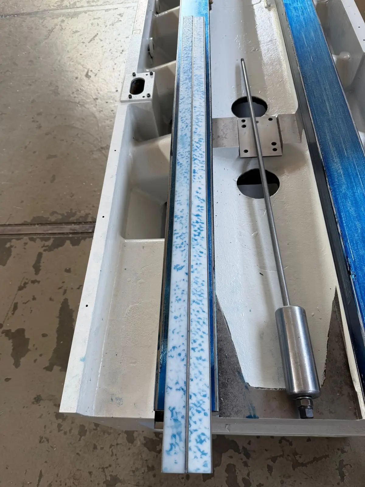 Weiß lackiertes Maschinenbett, eine schmale Leiste mit blauem Tragbild, rechts die durchgehend getuschte Bahn, dazwischen eine Kolbenstange.