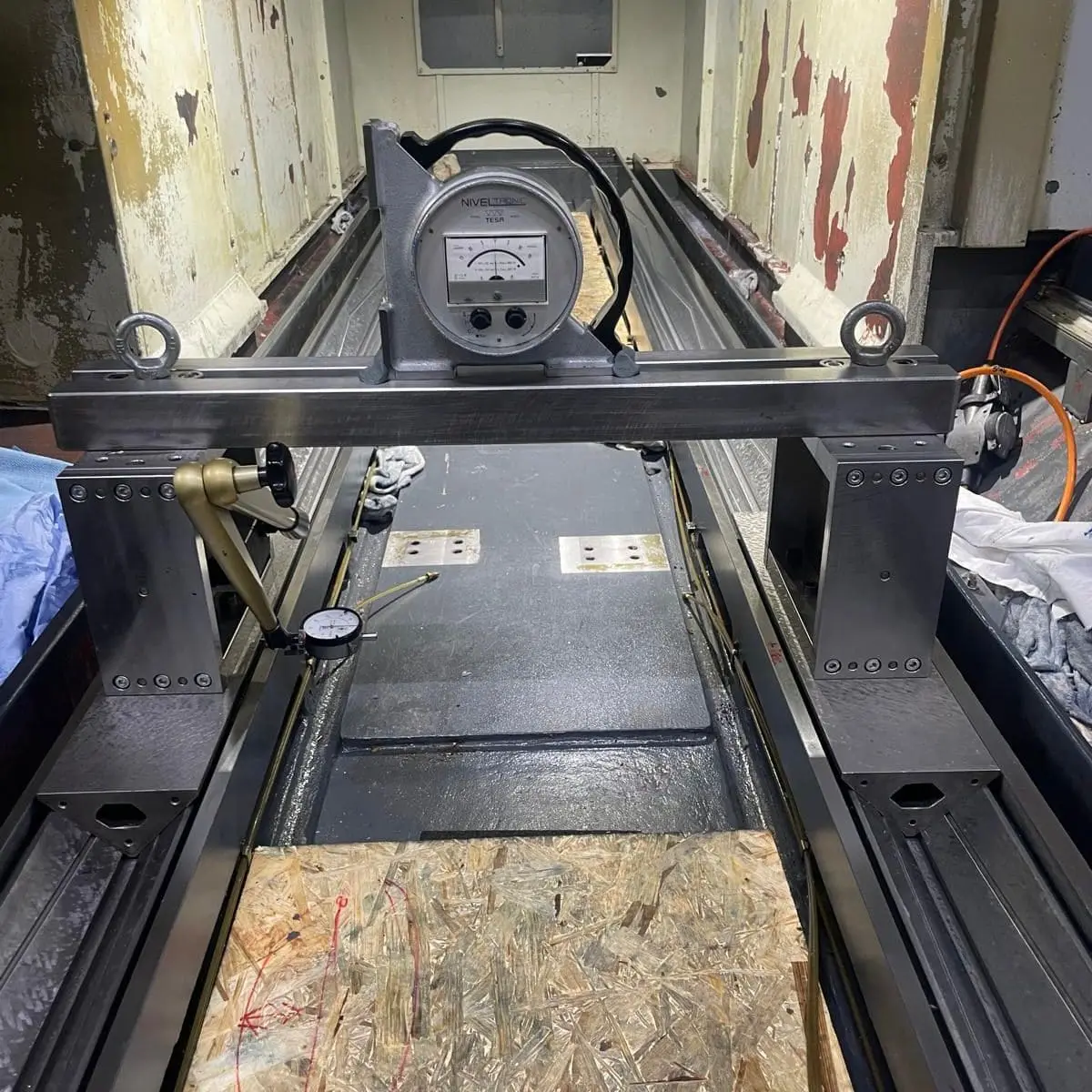 Messbrücke auf den Führungsbahnen im Inneren einer Maschine, darauf eine elektronische Libelle NIVELTRONIC, am Fuß eine Messuhr.