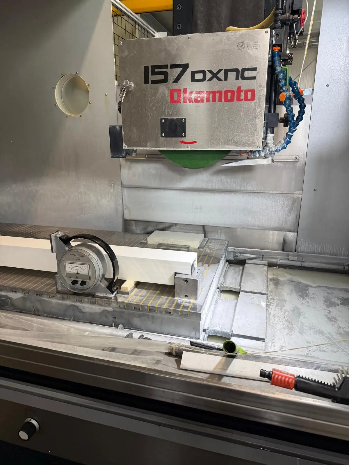 Elektronische Libelle NIVELTRONIC auf einem Präzisionslineal über dem Magnettisch einer Flachschleifmaschine, darüber das Schild Okamoto 157 DXNC.